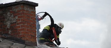 En brandman i skyddskläder och hjälm ovanpå ett hustak.